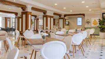 Un comedor de hotel con sillas y mesas blancas, vigas de madera en el techo y un letrero de 'Ilunion Hotels'.