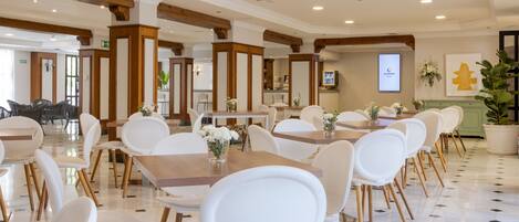 Une salle à manger d'hôtel avec des chaises et des tables blanches, des poutres en bois au plafond et une enseigne indiquant « Ilunion Hotels ».
