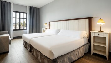 A hotel room with a double bed, a chair, a nightstand with a lamp, and a window with curtains.