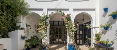 A courtyard with a white building, arched doorways, and potted plants.