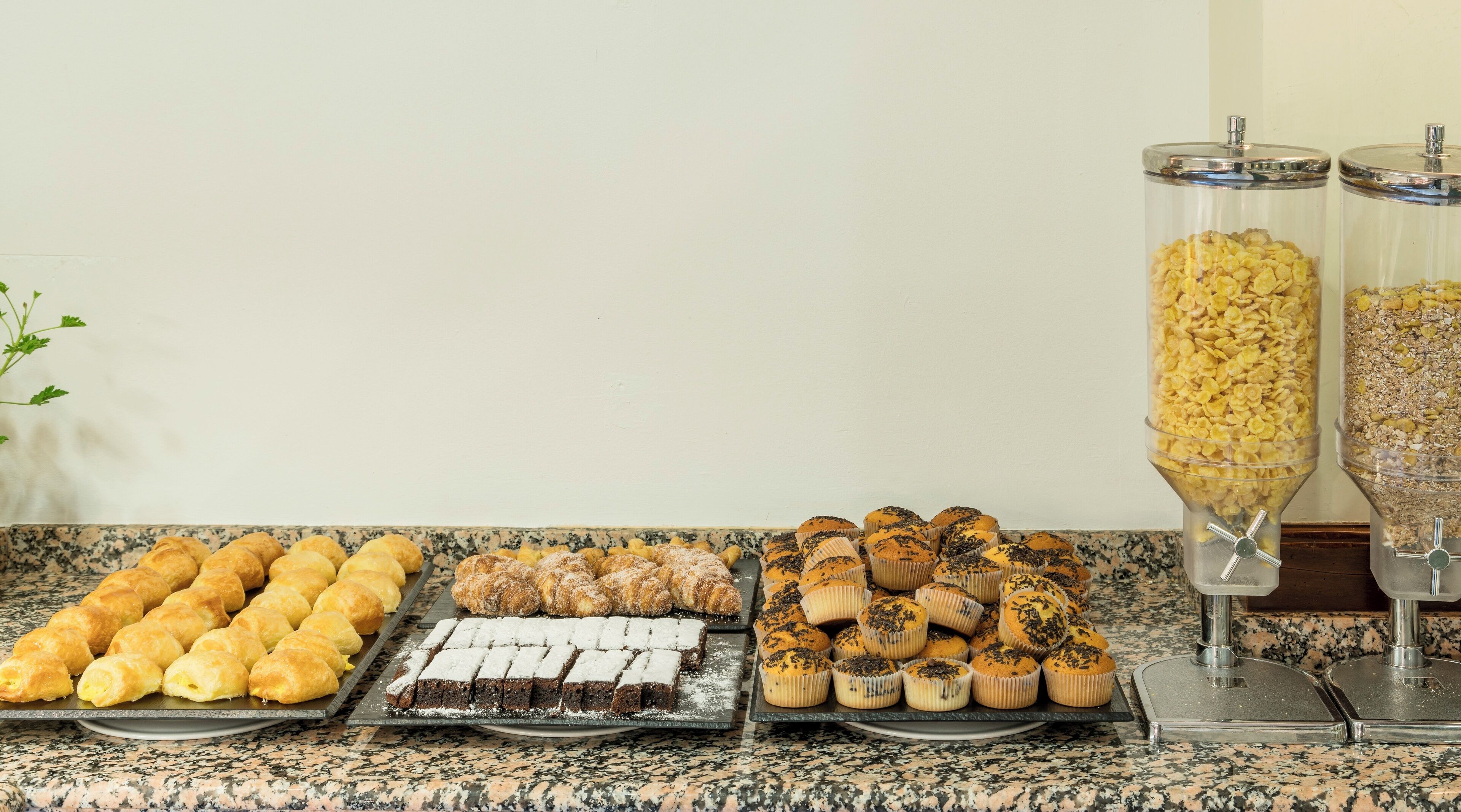 A buffet table with various baked goods including croissants, muffins, and brownies.