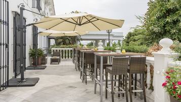 Un patio al aire libre con mesas y sillas, rodeado por una cerca blanca y follaje.