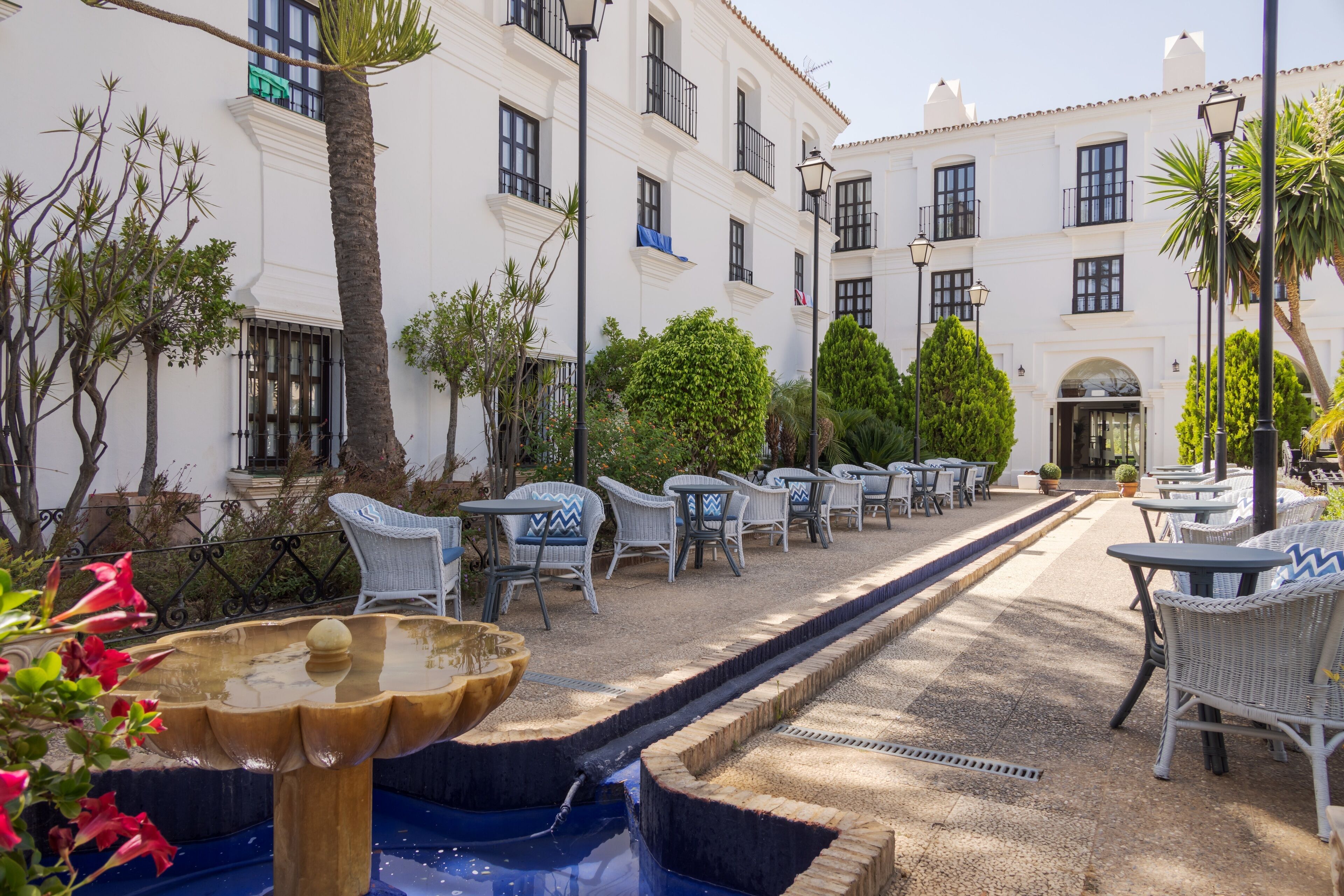 A courtyard with outdoor seating, a fountain, and a building with multiple windows and balconies.