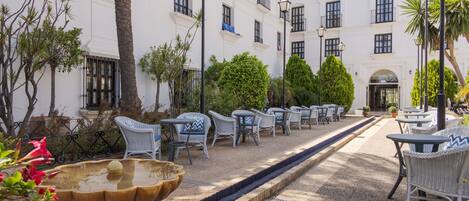 A courtyard with outdoor seating, a fountain, and a building with multiple windows and balconies.