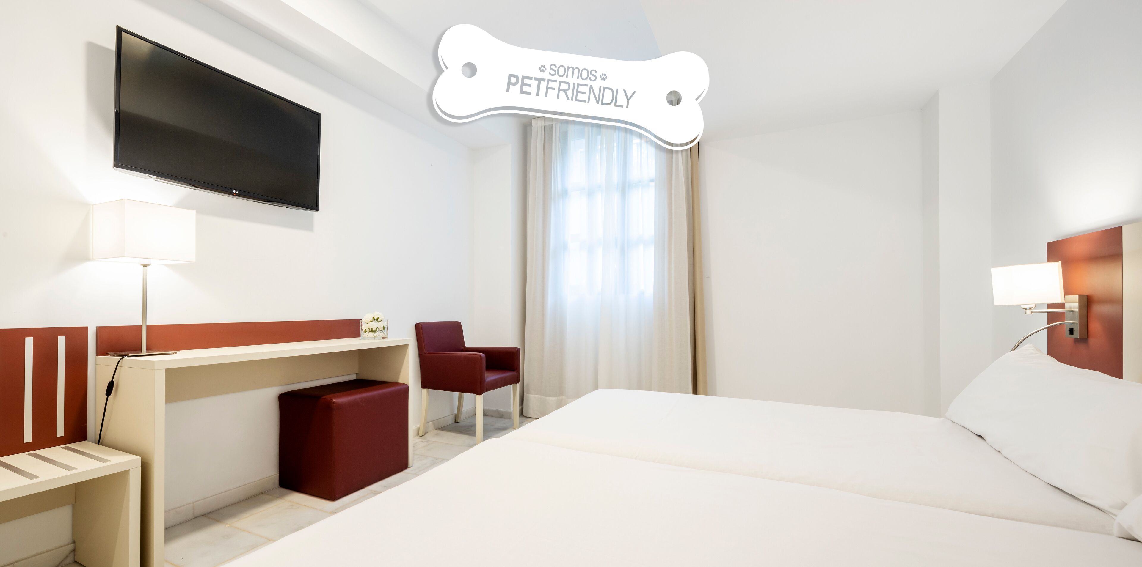 Habitación de hotel con cama, escritorio, silla, televisor y un cartel que dice 'Somos PETFRIENDLY'.