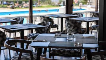 Un comedor con mesas y sillas, vistas a una piscina y un jarrón de vidrio sobre la mesa.