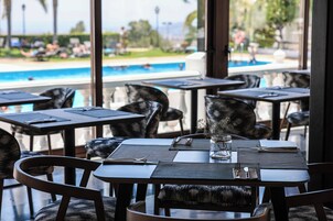 Un espace repas avec des tables et des chaises, une vue sur une piscine et un vase en verre posé sur la table.