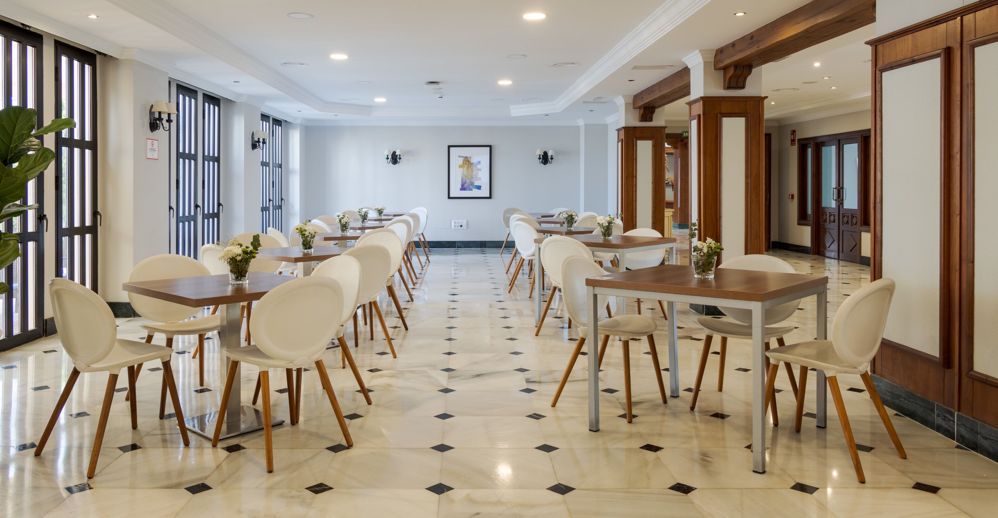 A spacious dining area with multiple tables and chairs, large windows, and a polished floor.