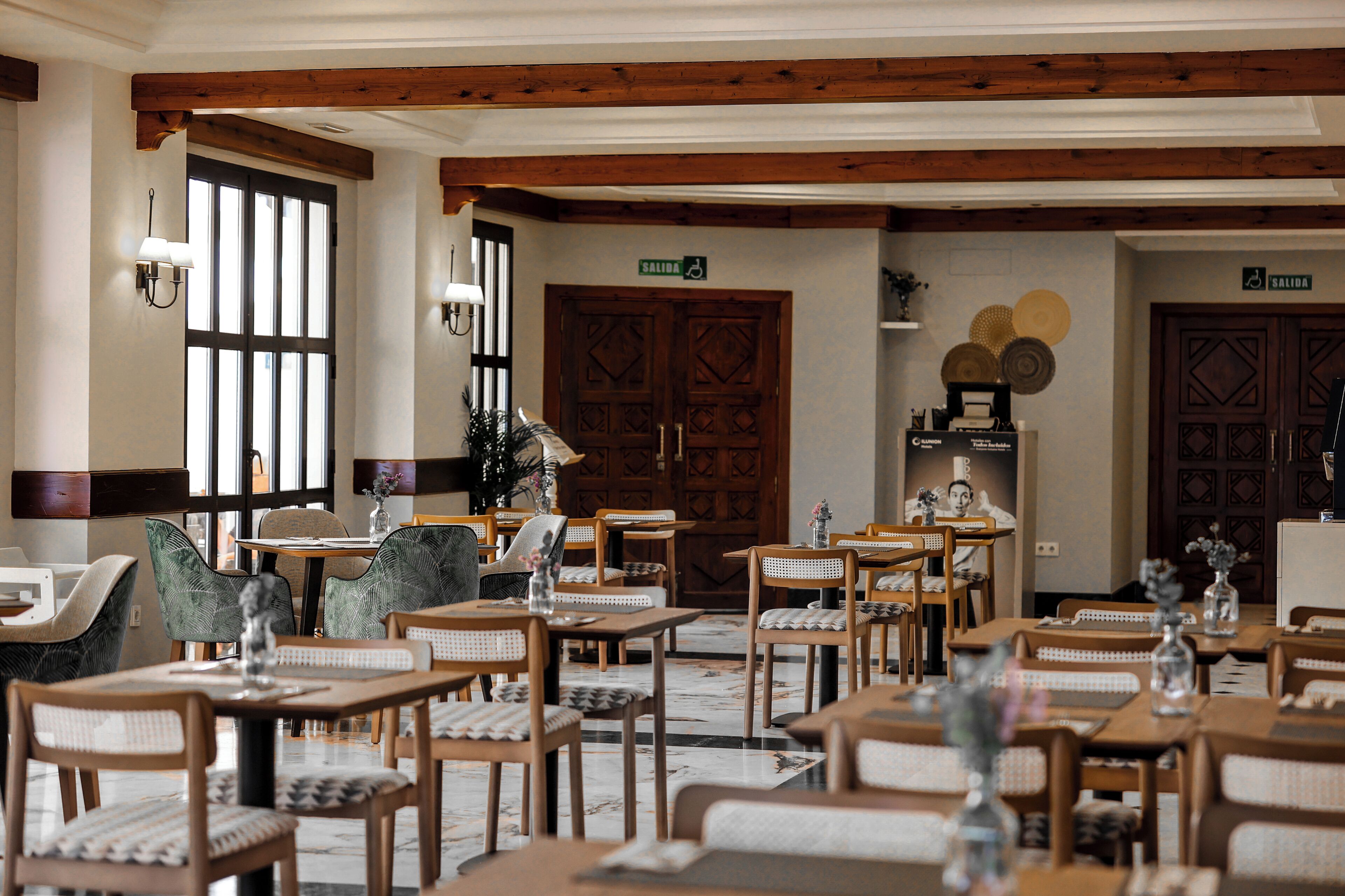 A restaurant with wooden tables and chairs, a large wooden door, and a sign indicating an exit.