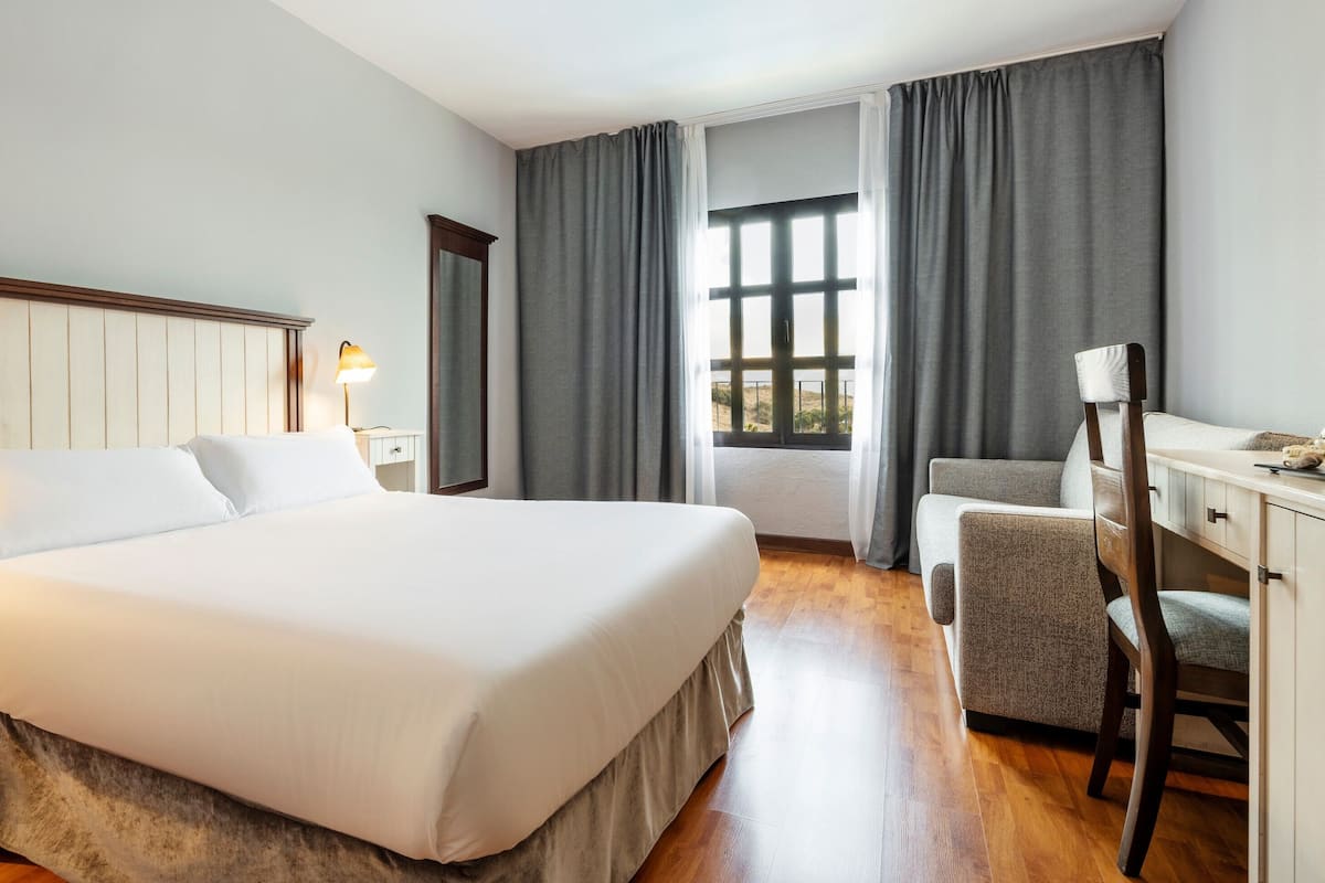 Quarto de hotel com cama grande, luminárias de cabeceira, escrivaninha e cadeira.