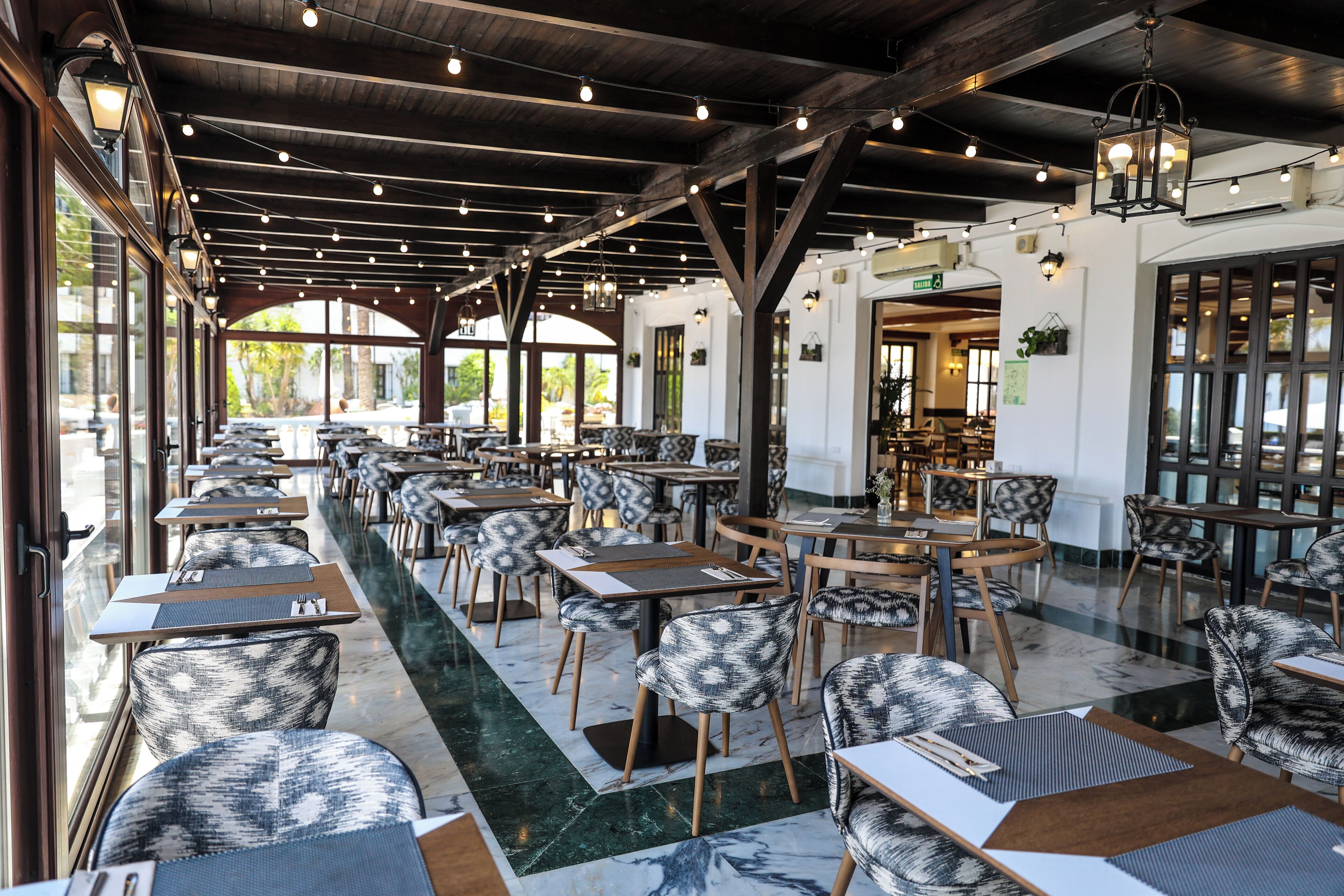 A spacious indoor dining area with high ceilings, wooden beams, and a long row of tables and chairs.