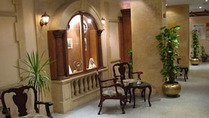 A lobby with a reception desk, two wooden chairs, a potted plant, and a decorative mirror. - Philippe Luxor Hotel (Luxor)
