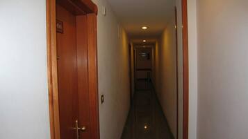 A narrow, well-lit hallway with wooden doors and a tiled floor, leading to a staircase.
