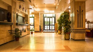 A hotel lobby with a reception desk, potted plants, and a large glass door leading outside. - Marhaba Hotel Aswan (Aswan)