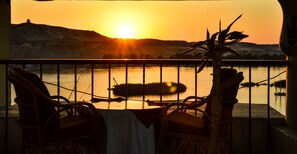 A balcony with wicker chairs and a table, overlooking a body of water with a sunset in the background. - Marhaba Hotel Aswan (Aswan)