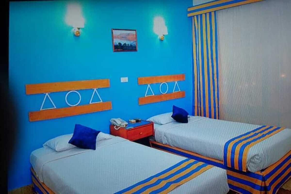 A hotel room with two beds, a nightstand, a telephone, and a window with curtains.