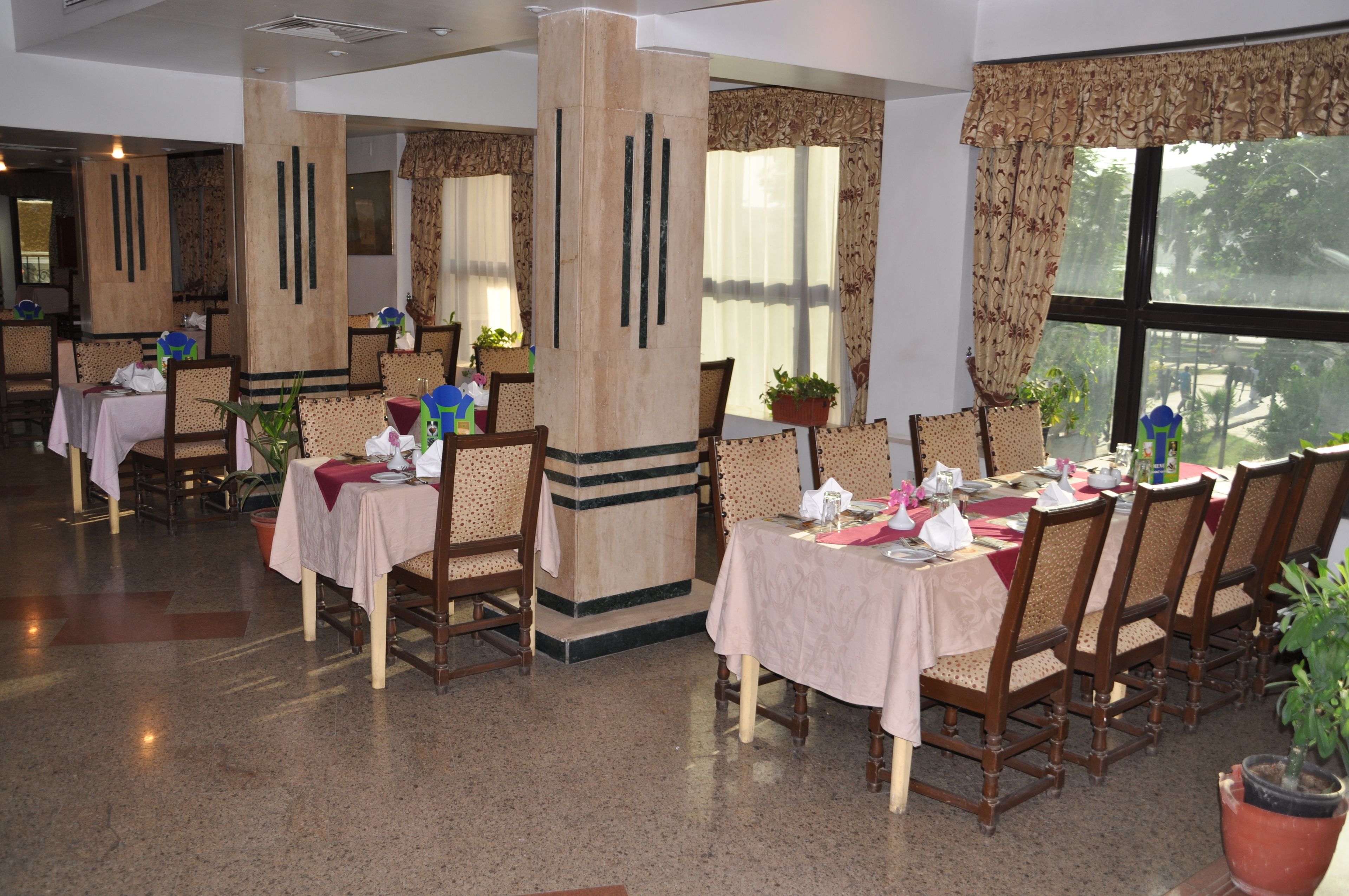 A dining area with tables set for service, chairs, and potted plants.