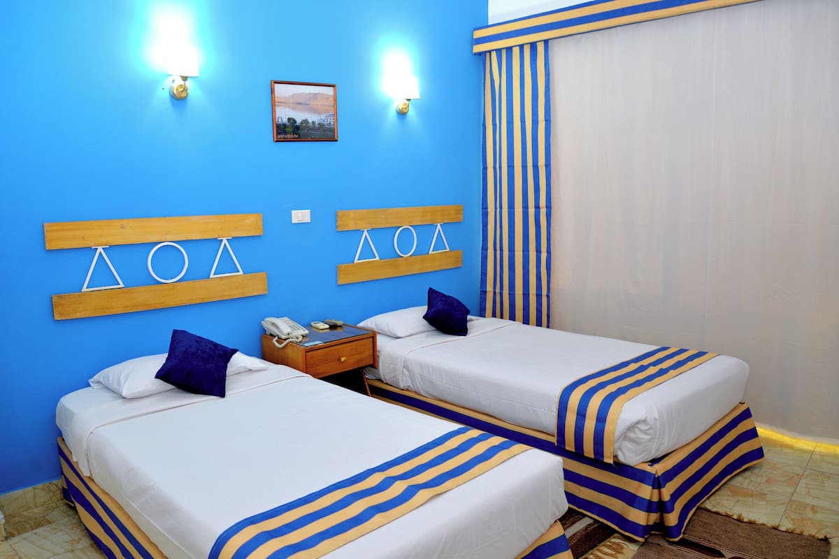 A hotel room with two beds, a wooden headboard, a nightstand, and a window with curtains.