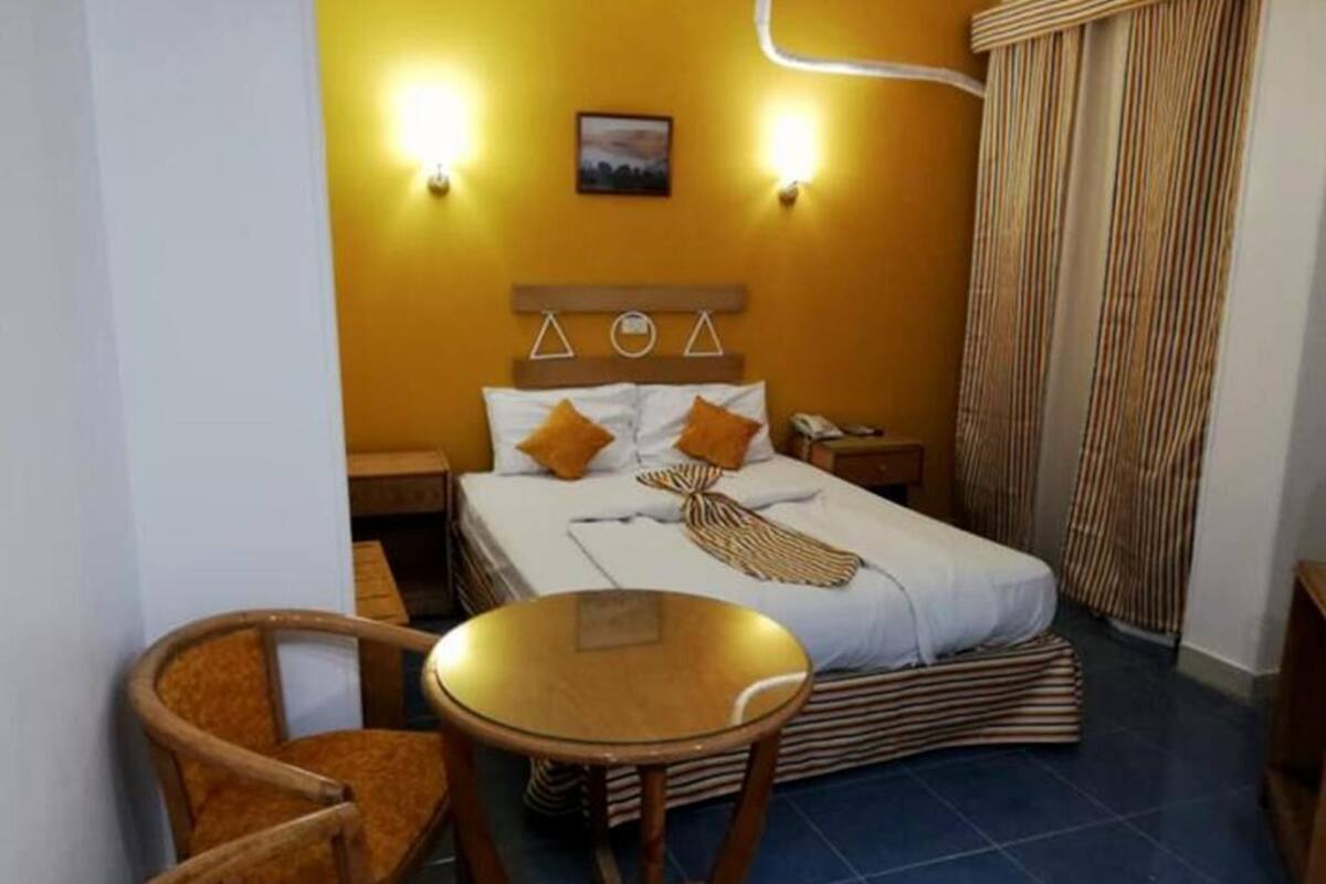 A hotel room with a bed, two bedside tables, a chair, a small round table, and a curtain.