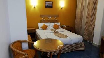 Habitación de hotel con una cama, dos mesitas de noche, una silla, una mesita redonda y una cortina.