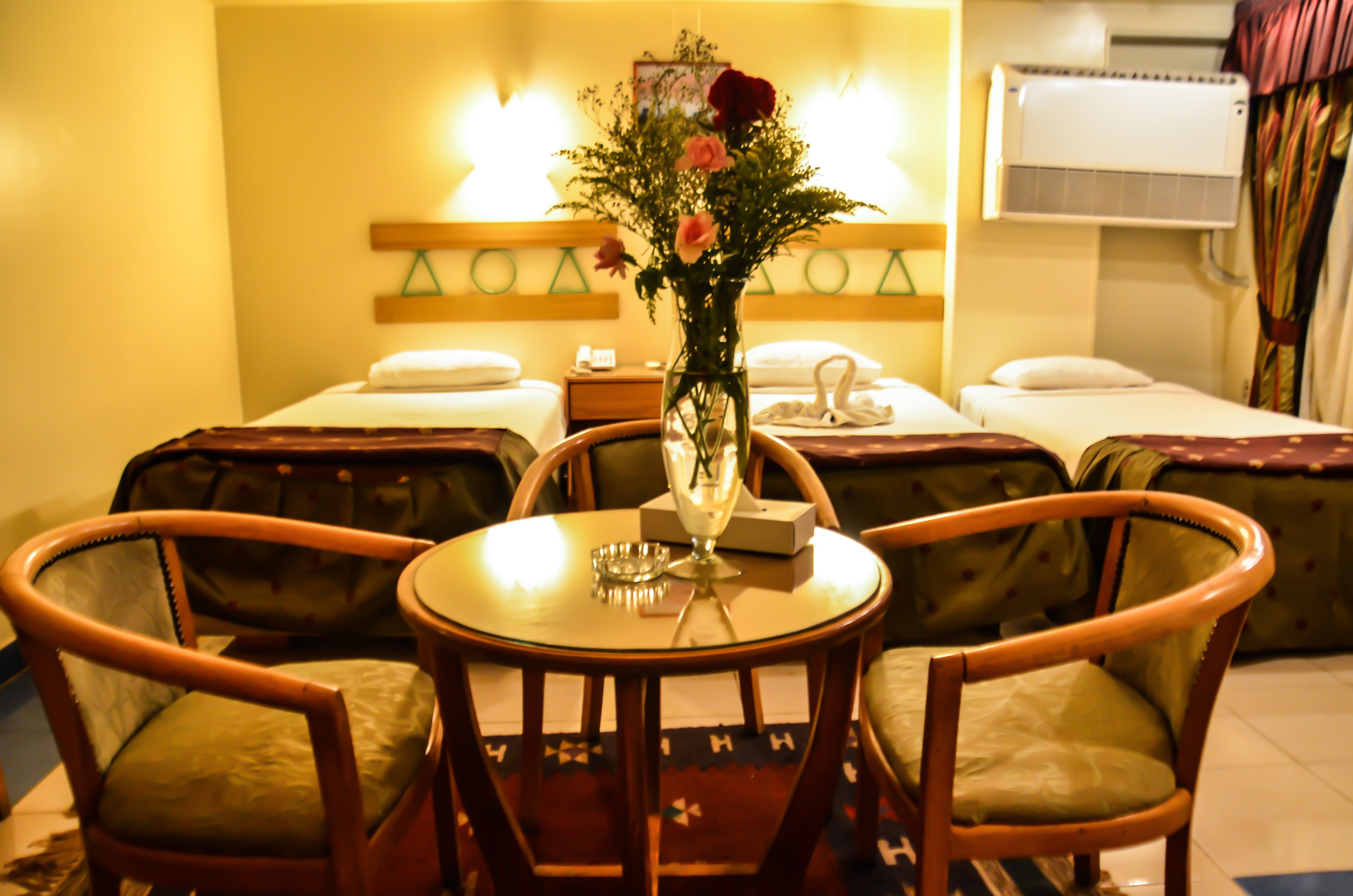 Ein Hotelzimmer mit zwei Einzelbetten, einem kleinen Tisch mit Blumen in einer Vase und zwei Holzstühlen.