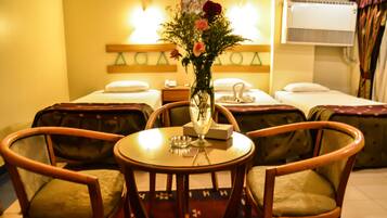 Ein Hotelzimmer mit zwei Einzelbetten, einem kleinen Tisch mit Blumen in einer Vase und zwei Holzstühlen.