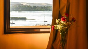 A window with a view of a river and boats, a vase with red flowers, and a curtain. - Marhaba Hotel Aswan (Aswan)