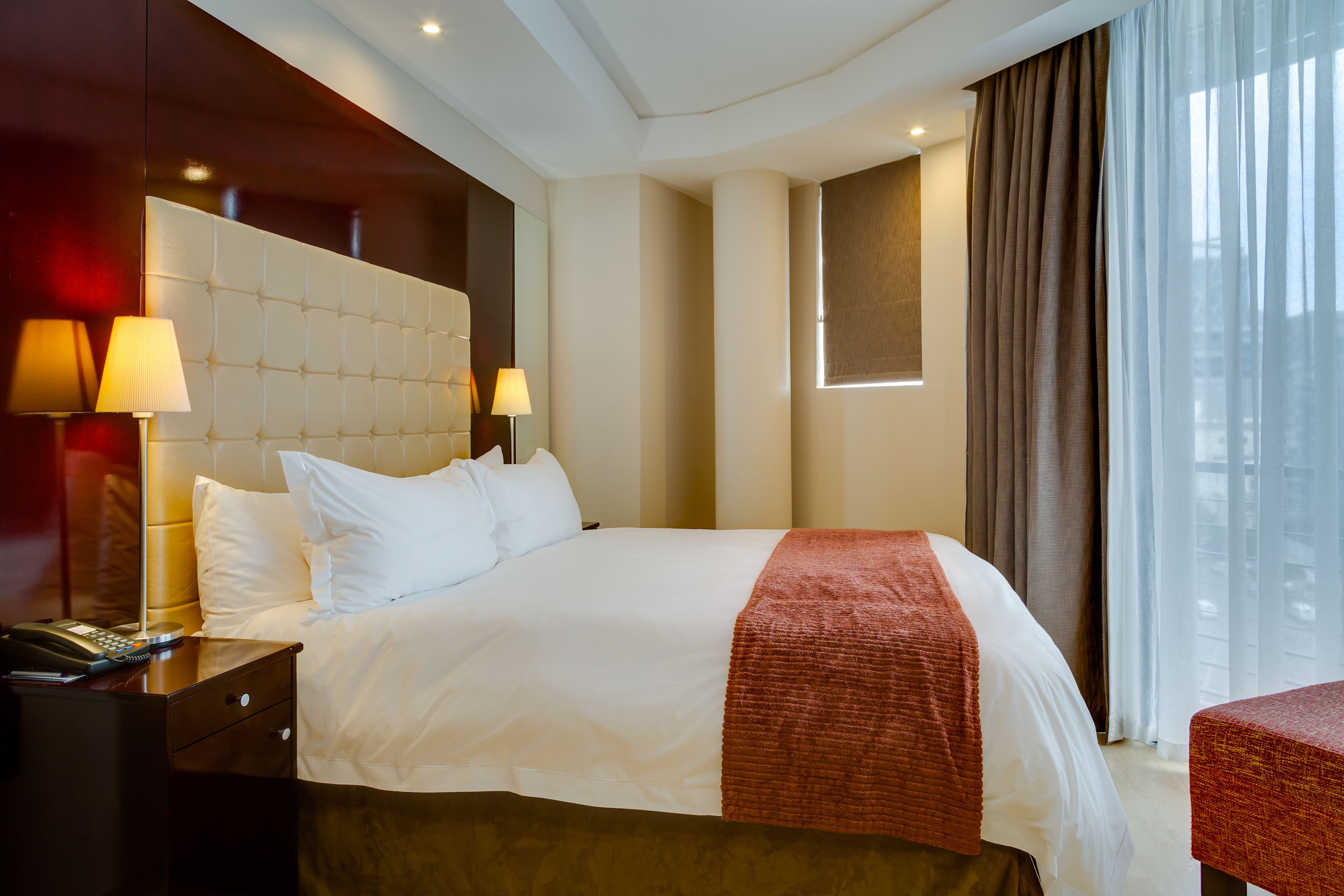 Habitación de hotel con una cama grande, dos lámparas de noche, una mesita de noche con teléfono y una ventana con cortinas.