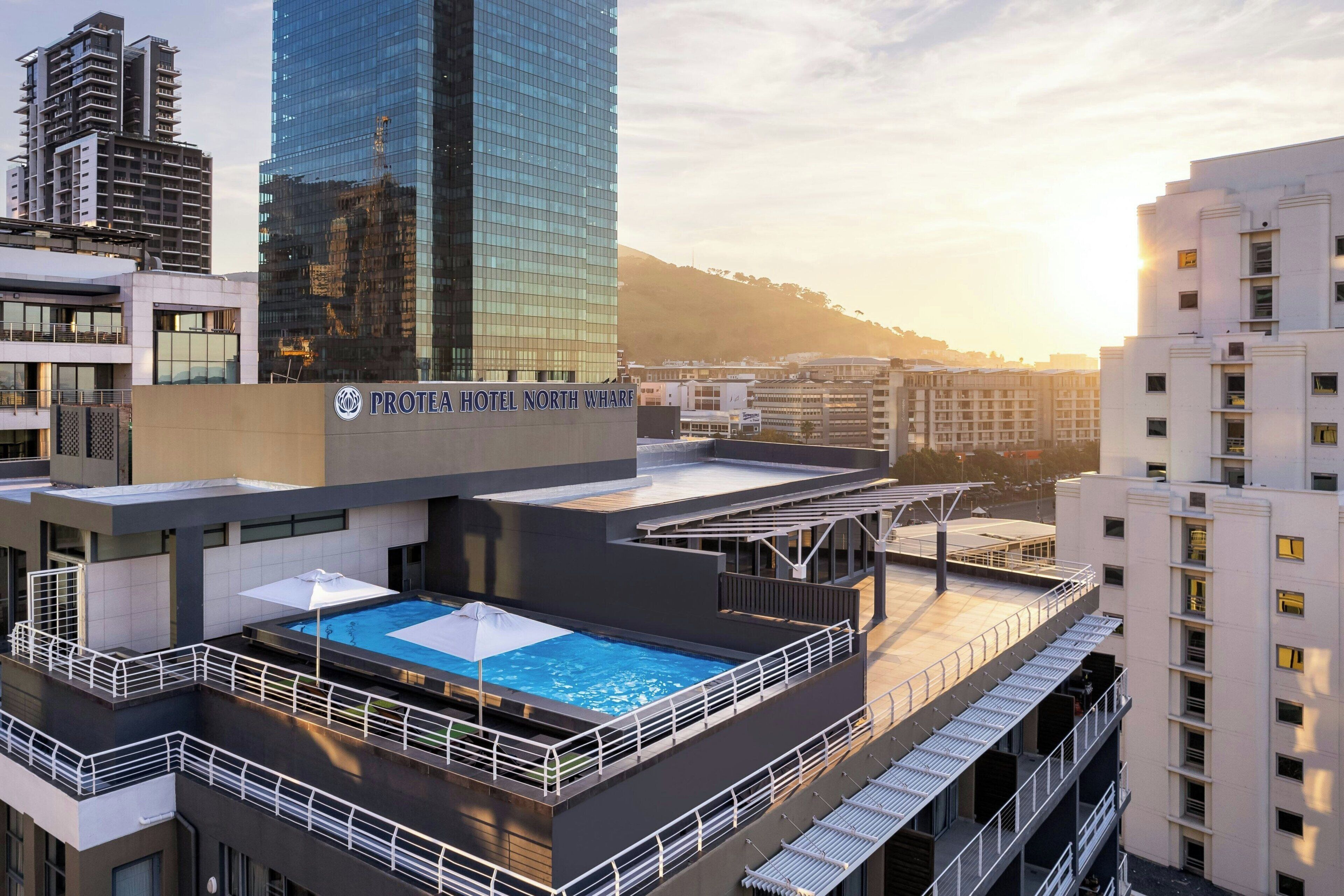 A hotel with a rooftop pool, modern architecture, and a view of surrounding buildings.