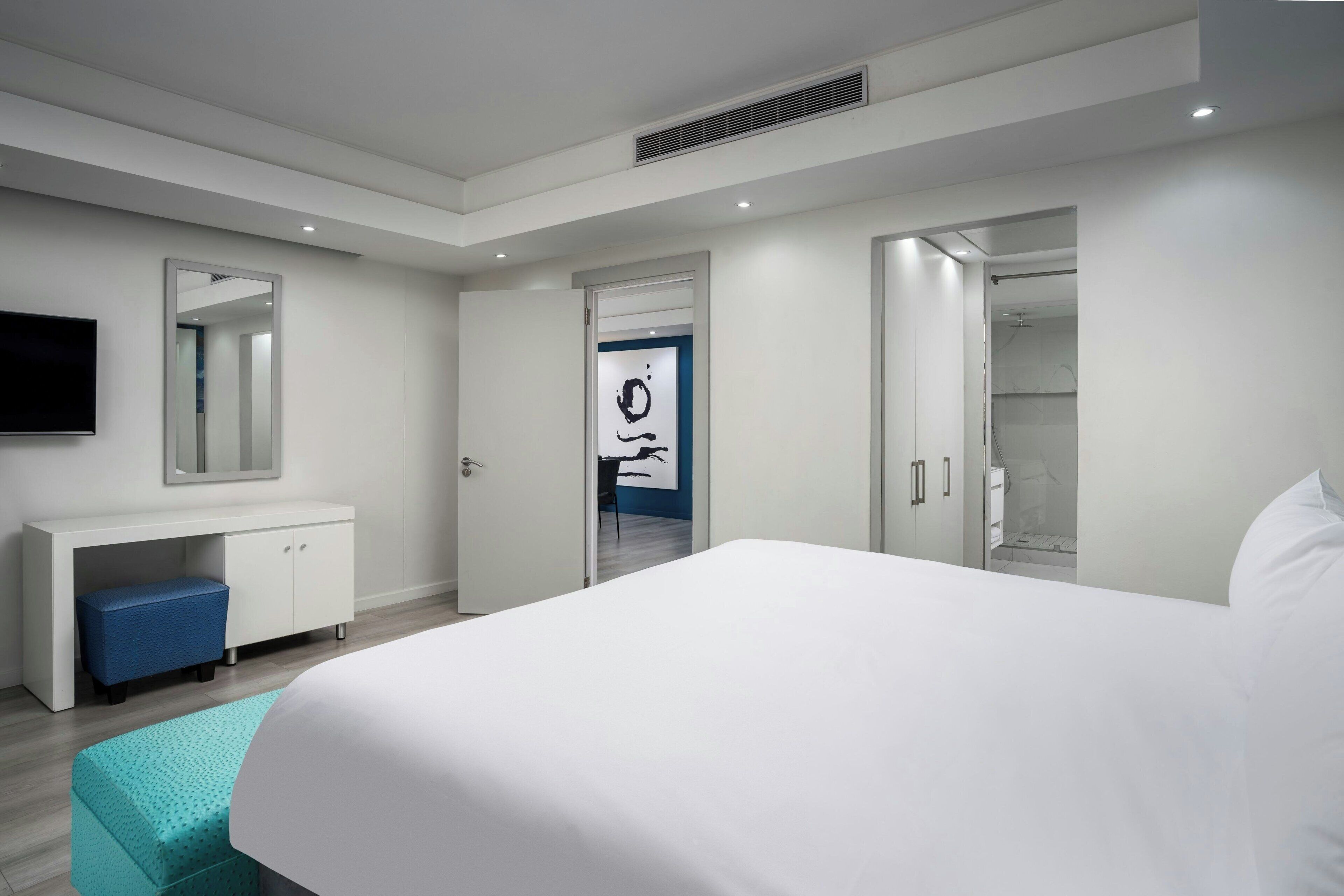 A modern hotel room with a large bed, a desk, a mirror, and a walk-in closet.