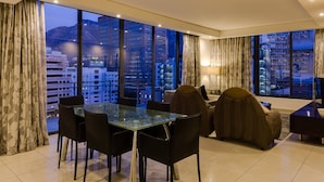 A modern hotel room with a dining area, large windows, and a view of the cityscape.