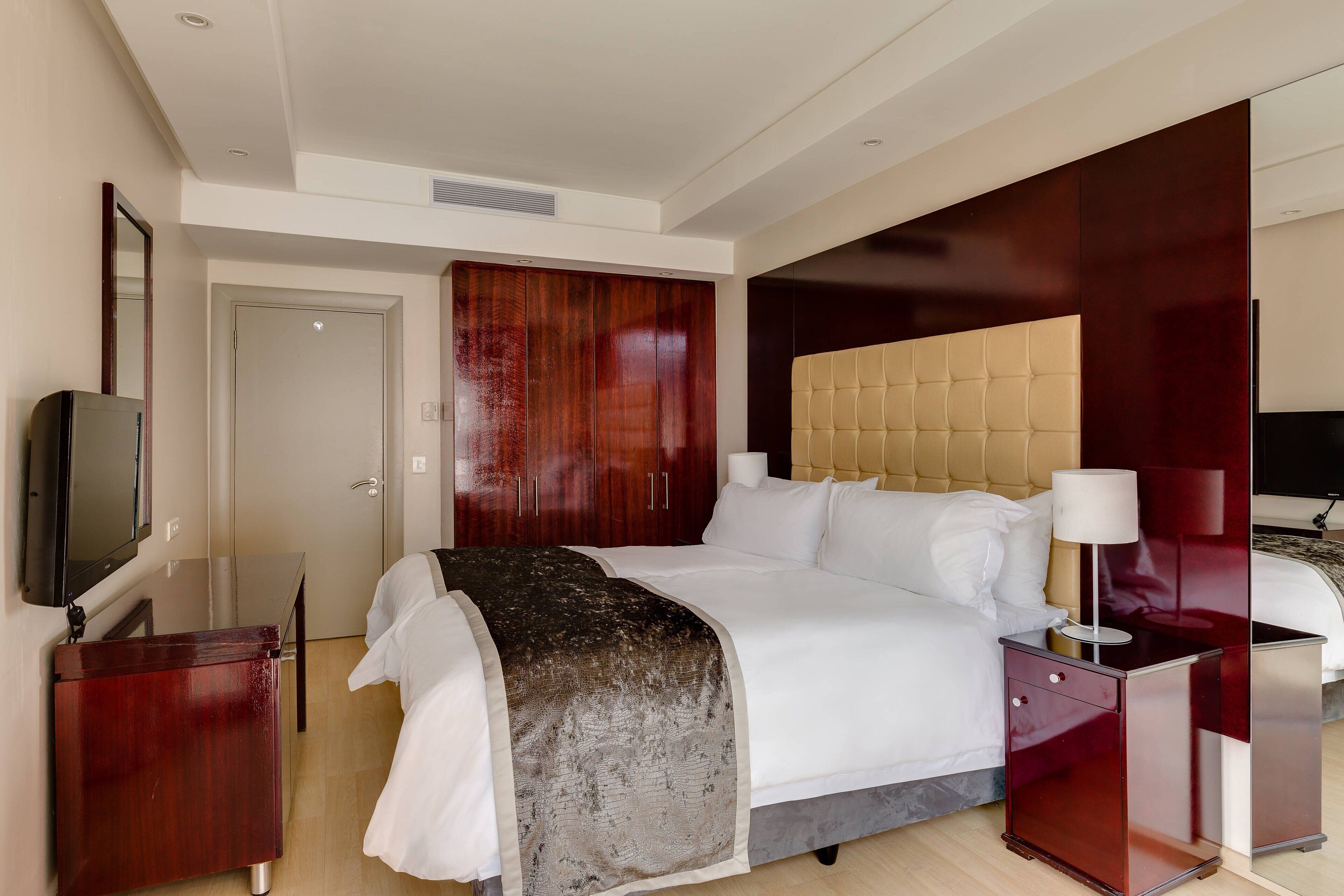 Une chambre d’hôtel moderne avec un grand lit, une armoire en bois, une télévision et une table de chevet avec une lampe.