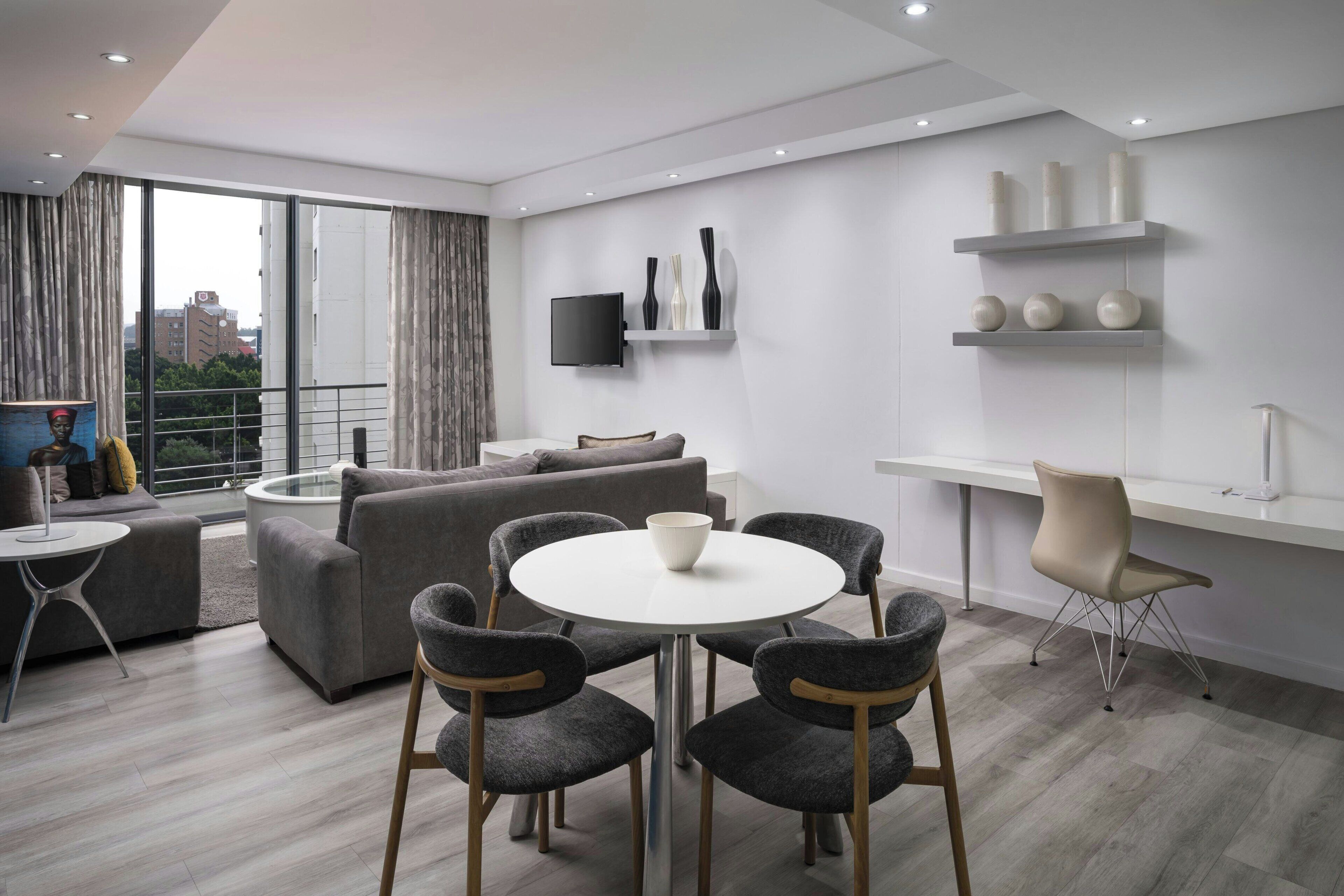 A modern living room with a round dining table, grey sofas, and a TV mounted on the wall.