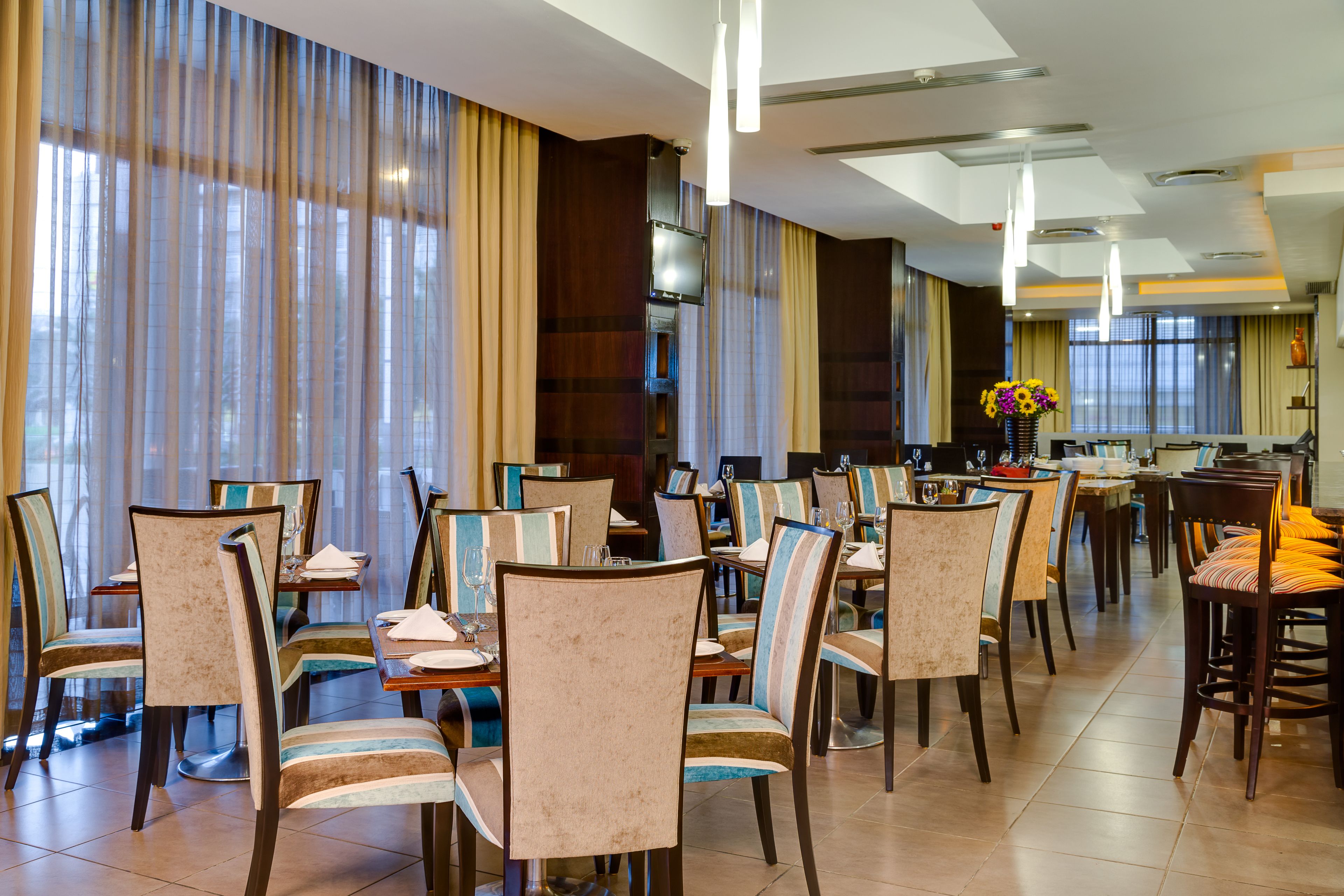 Un vaste espace dédié à la salle à manger, avec de nombreuses tables et chaises, de grandes fenêtres dotées de rideaux et un éclairage moderne.