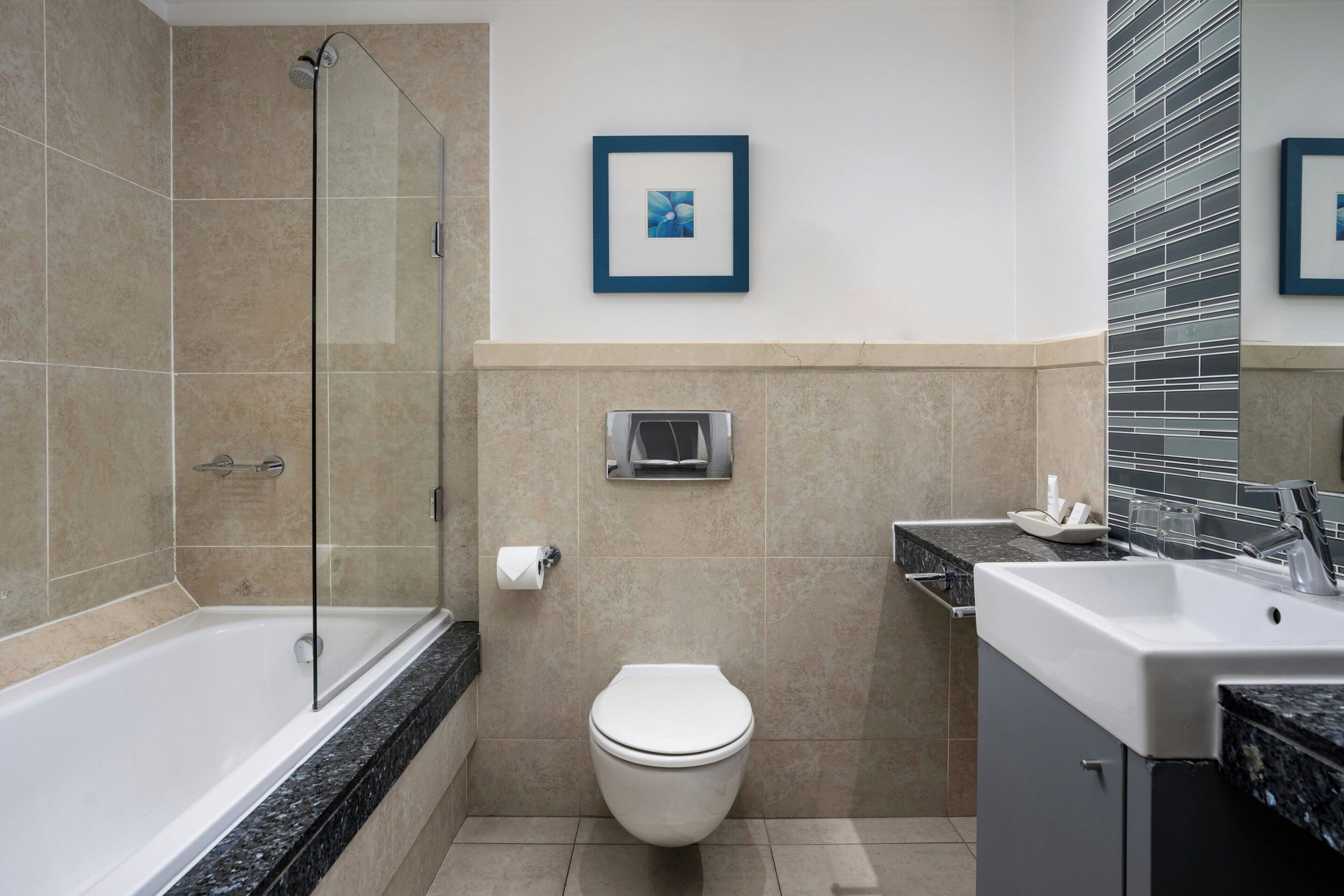 A modern bathroom with a shower, toilet, sink, and a framed picture on the wall.