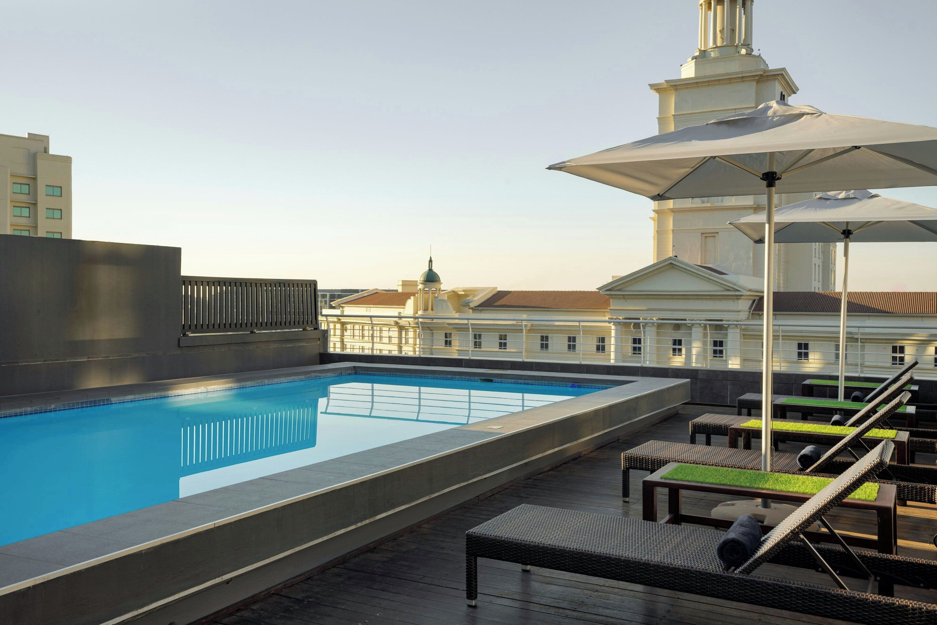 A rooftop swimming pool with lounge chairs and umbrellas, surrounded by buildings.