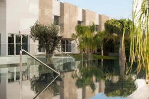 A modern building with a reflective pool, surrounded by palm trees and a small tree.