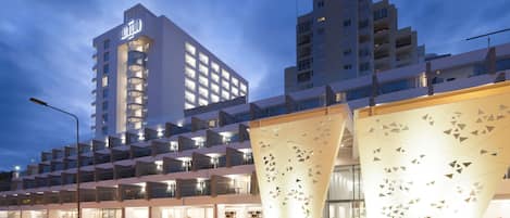 A modern hotel with a prominent tower, multiple balconies, and a distinctive entrance with geometric cutouts.
