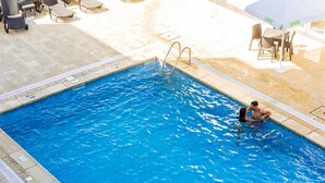 A swimming pool with a metal ladder, lounge chairs, and a table with umbrellas. - MS Vila Nova (Ponta Delgada)