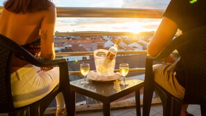 Two people seated at a table with a bottle of champagne and two glasses on a balcony overlooking a cityscape. - MS Vila Nova (Ponta Delgada)