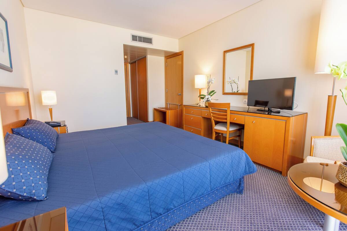 Une chambre d’hôtel avec un grand lit, un bureau avec un ordinateur, une chaise et une petite table avec une lampe.