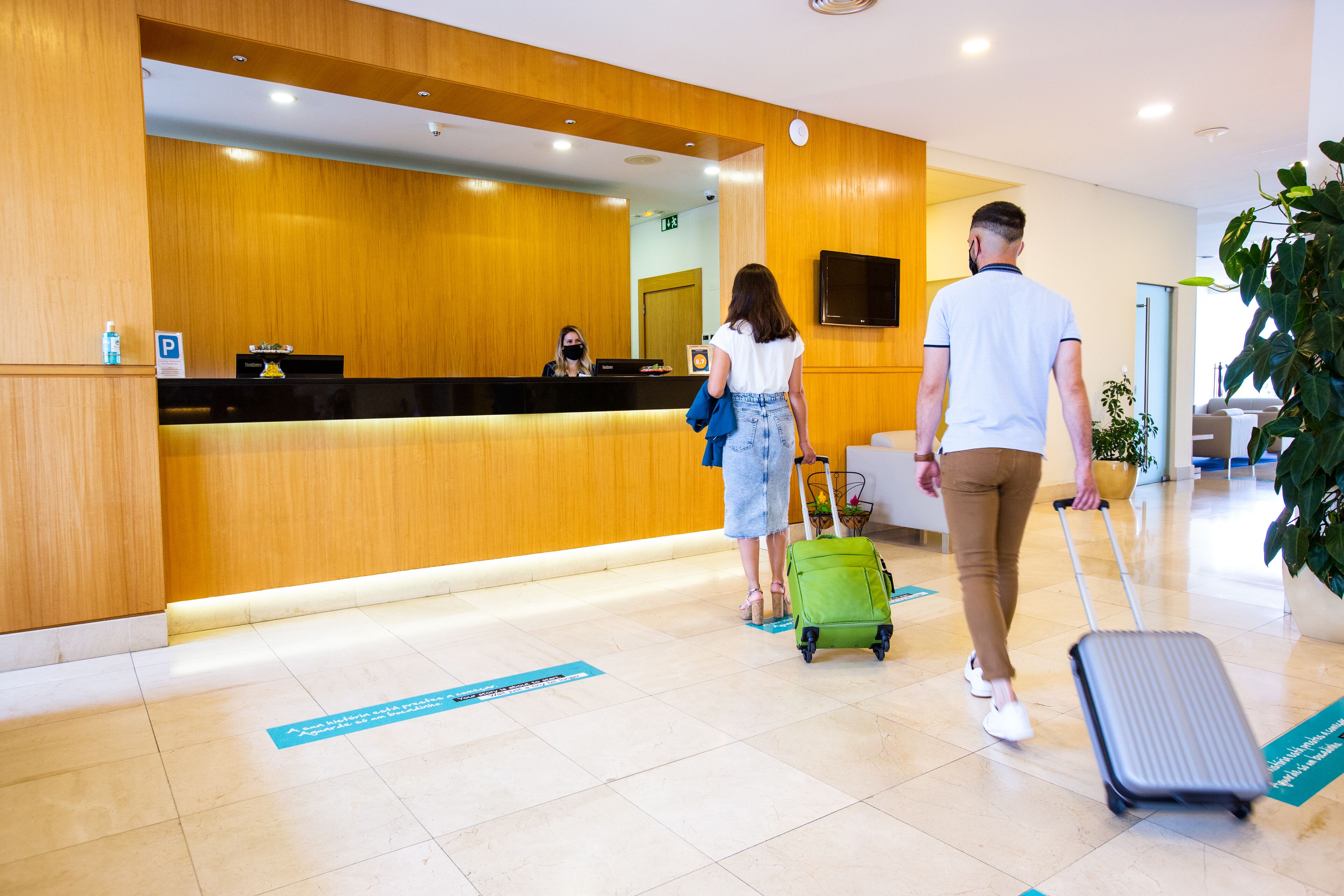 A reception area with a wooden reception desk, a digital screen, and a potted plant.