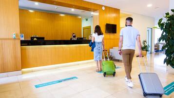 A reception area with a wooden reception desk, a digital screen, and a potted plant.