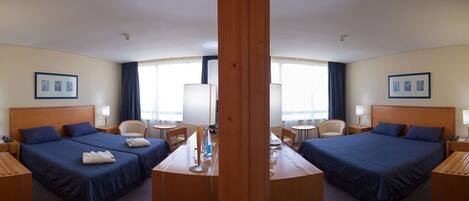 A hotel room with two beds, a central table, and a large window.