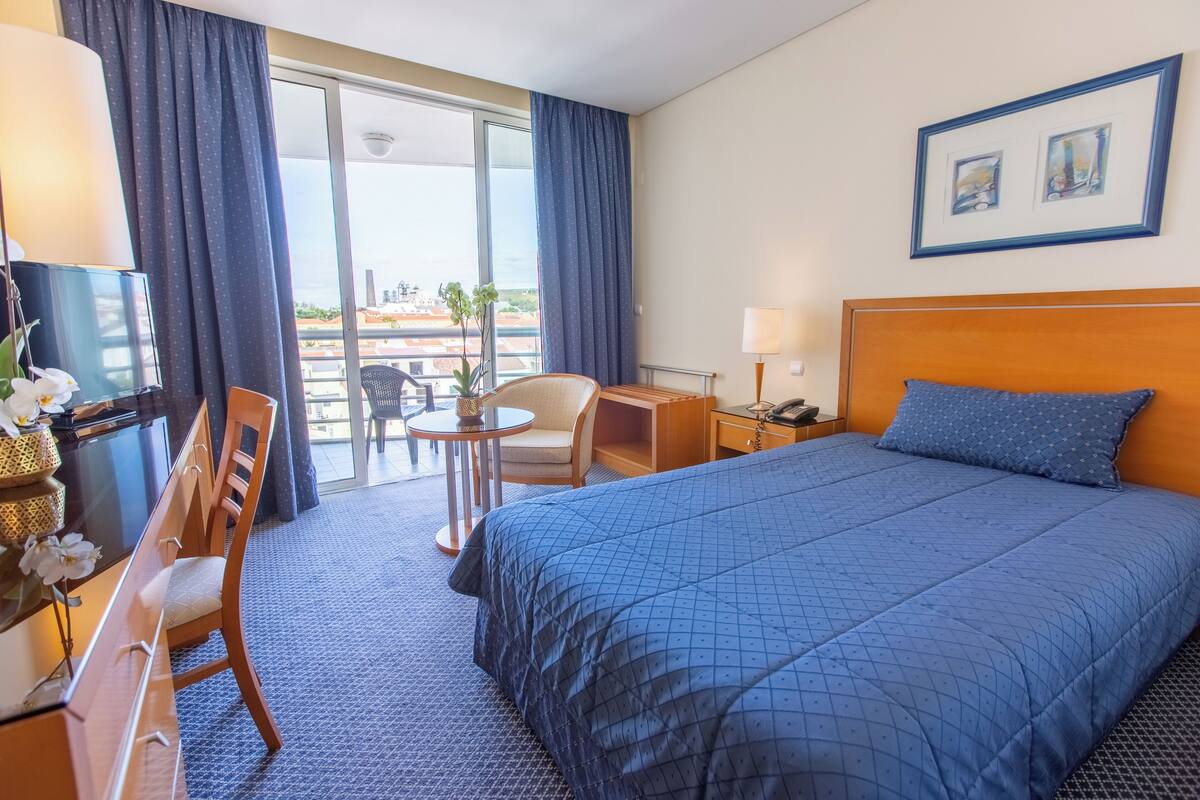 Une chambre d’hôtel avec un grand lit, un bureau, une chaise, une petite table et un balcon avec vue.