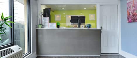 A modern hotel lobby with a reception desk, a large window, and a welcome mat.