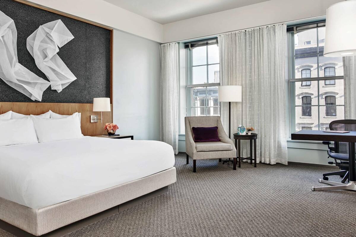 A hotel room with a large bed, a chair, a desk, and a window with curtains.