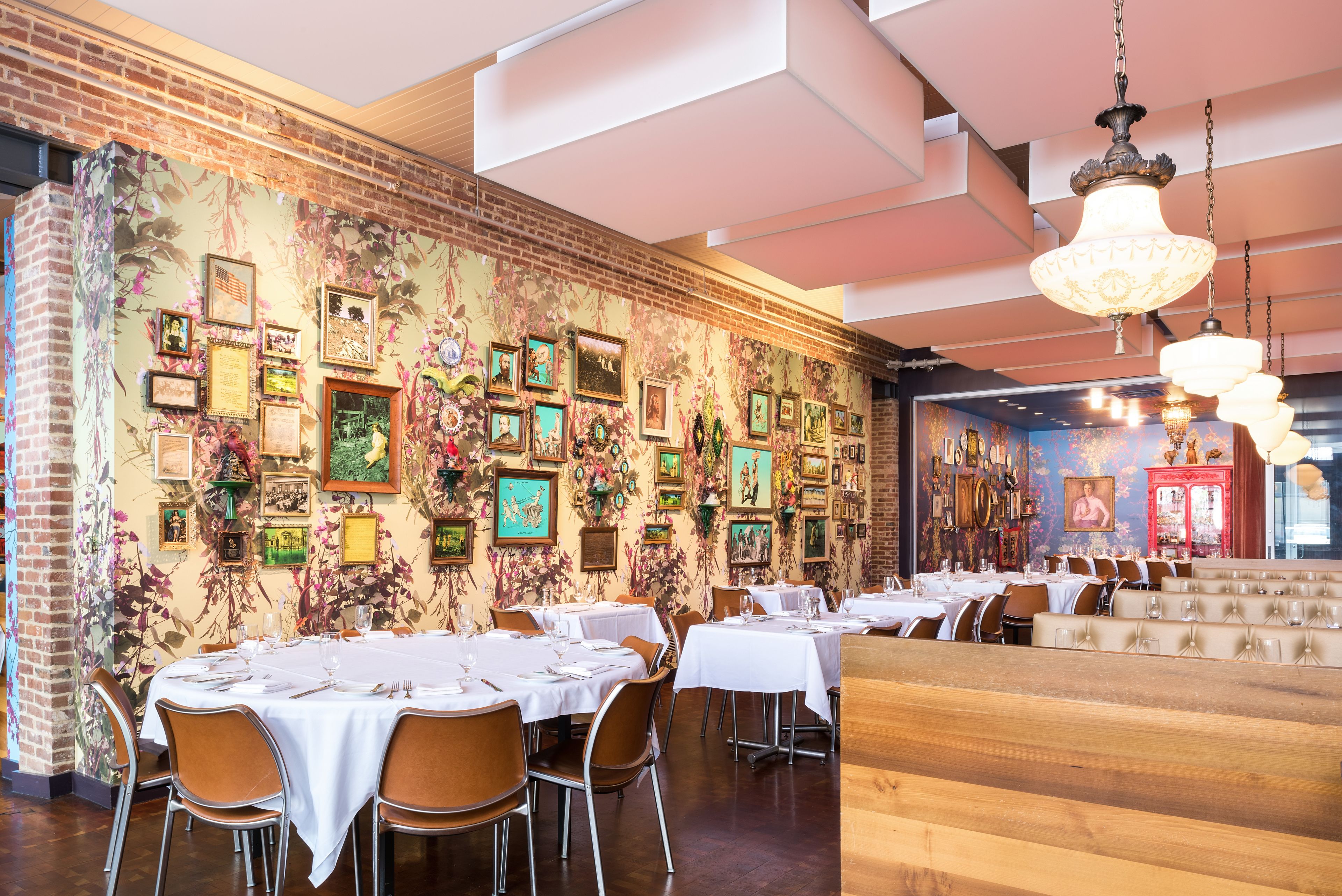 A restaurant with brick walls, framed pictures, and white tables set for dining.