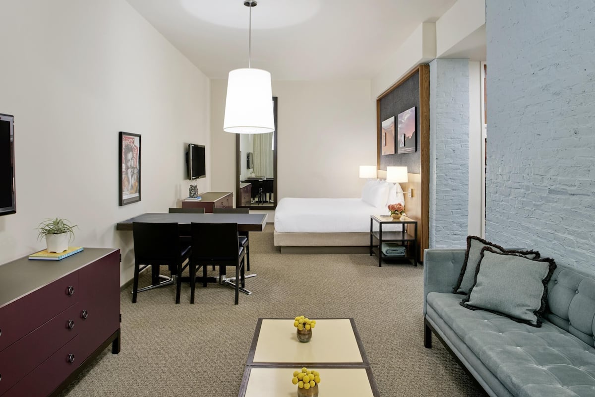 A hotel room with a bed, desk, chair, dresser, and a sofa.
