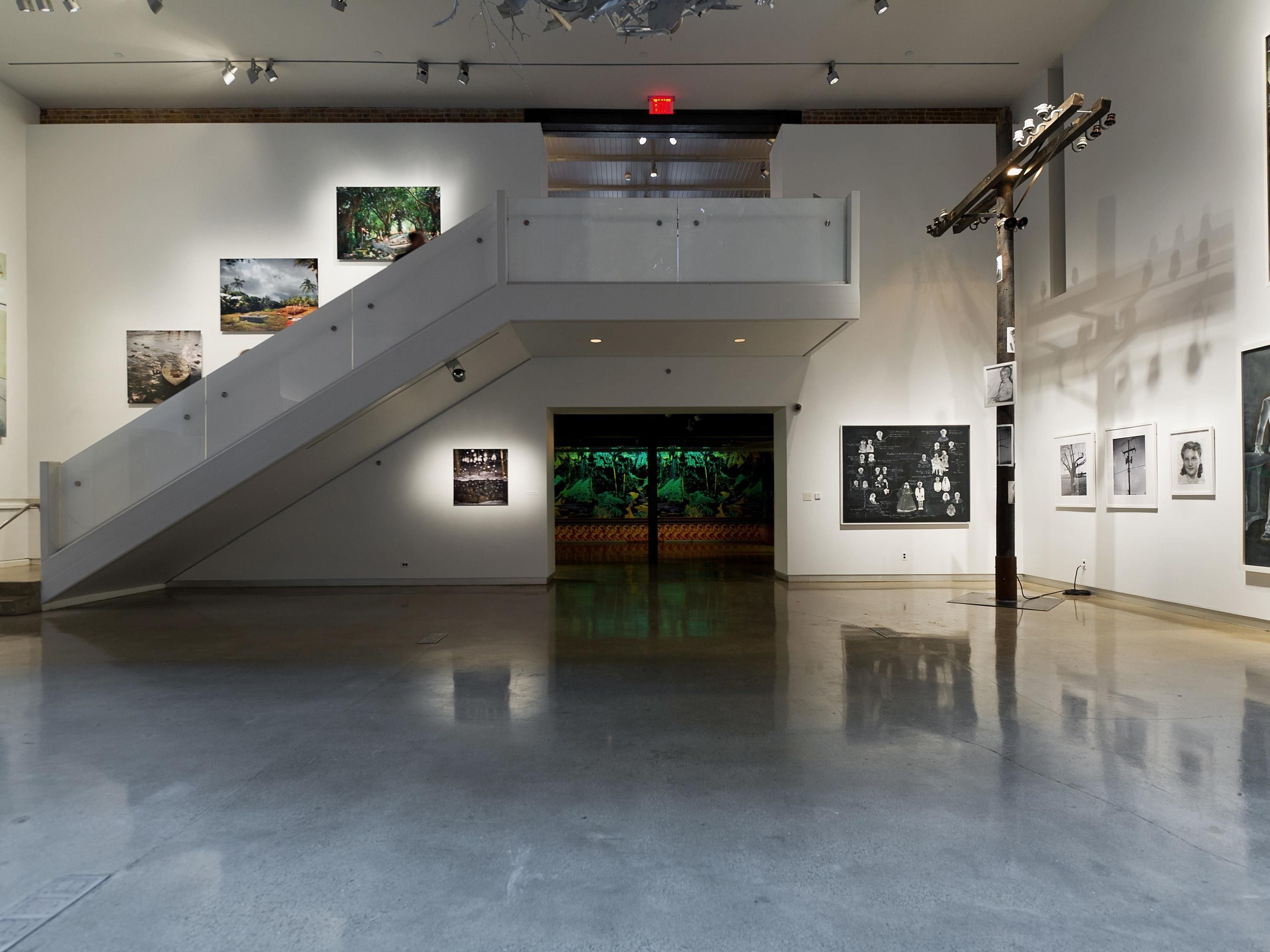 A spacious gallery with a central staircase, artwork on the walls, and a reflective floor.